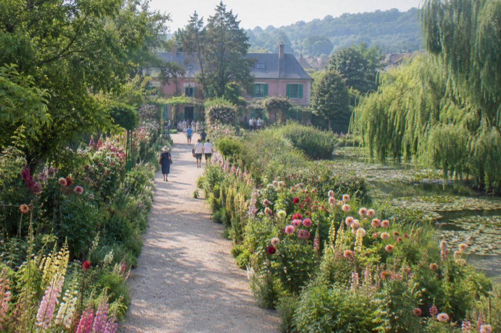 Visitors walking a broad gravel alley bordered by tall flower beds in a formal garden