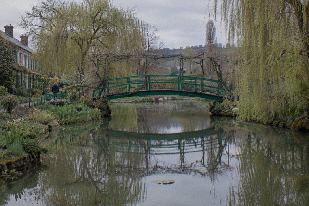 A green metal footbridge over the water lily pond in Monet's garden, surrounded by willows