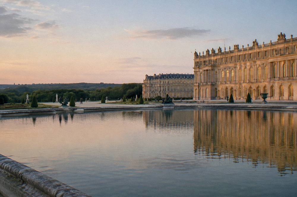 A gilded palace facade reflected across a wide formal garden terrace