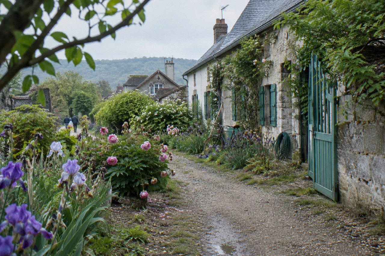 A flower-lined garden path leading toward a stone house facade in a Normandy village