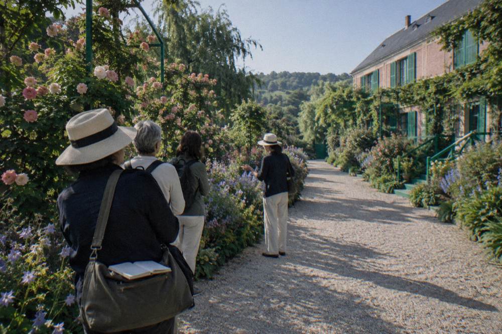 Small tour group gathered on a garden path beside flowering beds at Giverny