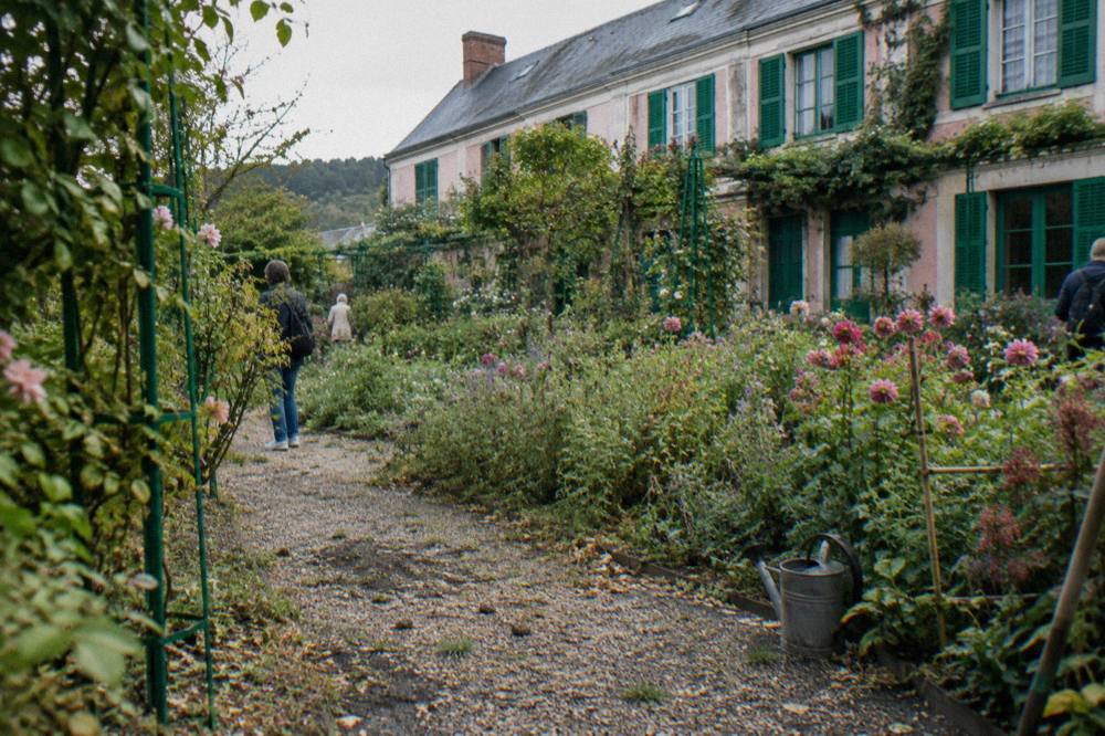 Row of flower beds and the pink facade of Monet's house seen across the Clos Normand garden