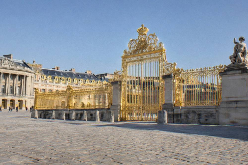 Golden gates and stone facade of the Palace of Versailles under a clear sky