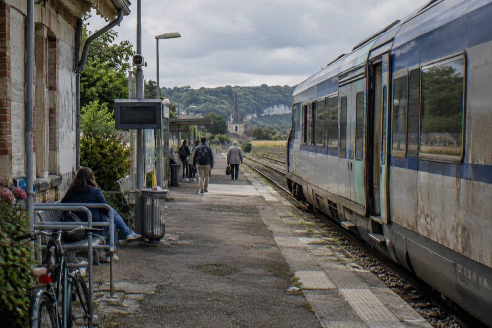 A regional train waiting at a country station platform beside open fields