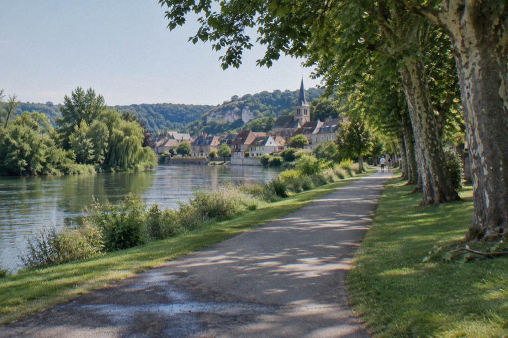 A paved green cycling path running beside the Seine toward a small village