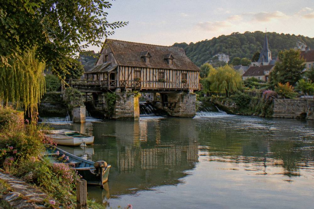 The Seine river flowing past green banks near Vernon with a riverside mill in the distance