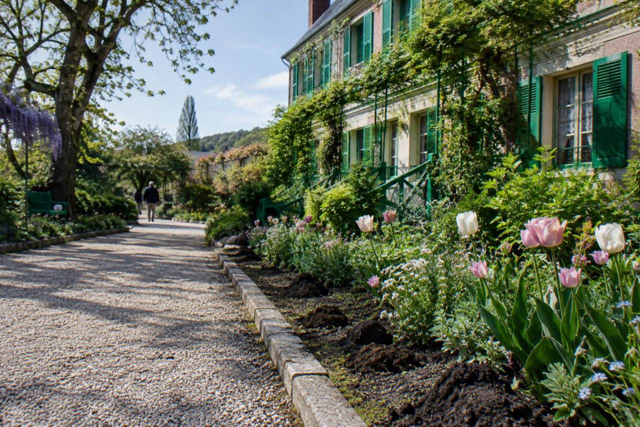 A flower-lined gravel path leading toward the pink facade of Monet's house in Giverny