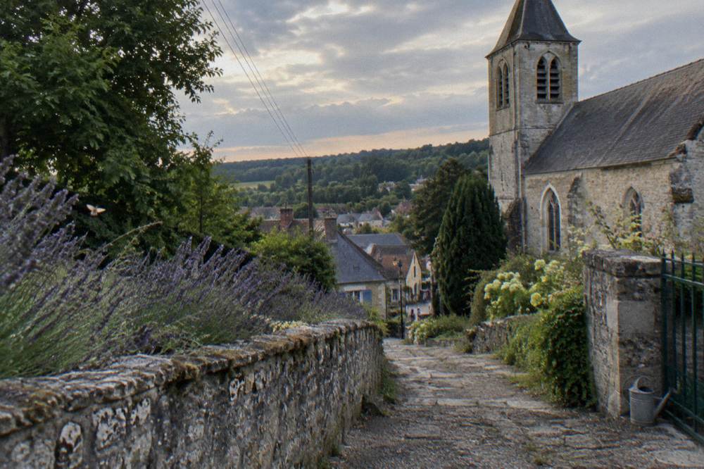 A stone path beside a garden wall leading toward the church in Giverny
