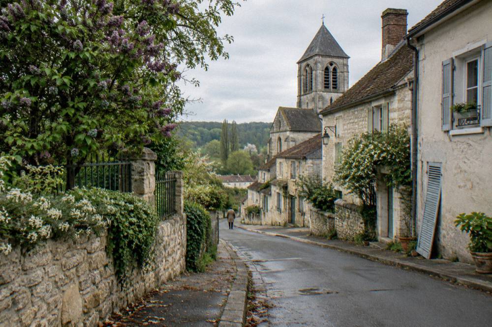 A narrow village street of stone houses with a gray stone church tower rising above the rooftops