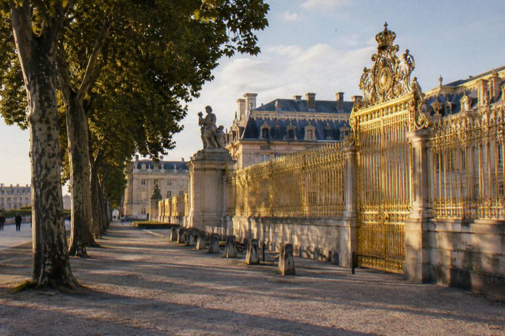 Park path beside an ornate gilded palace gate in late afternoon light