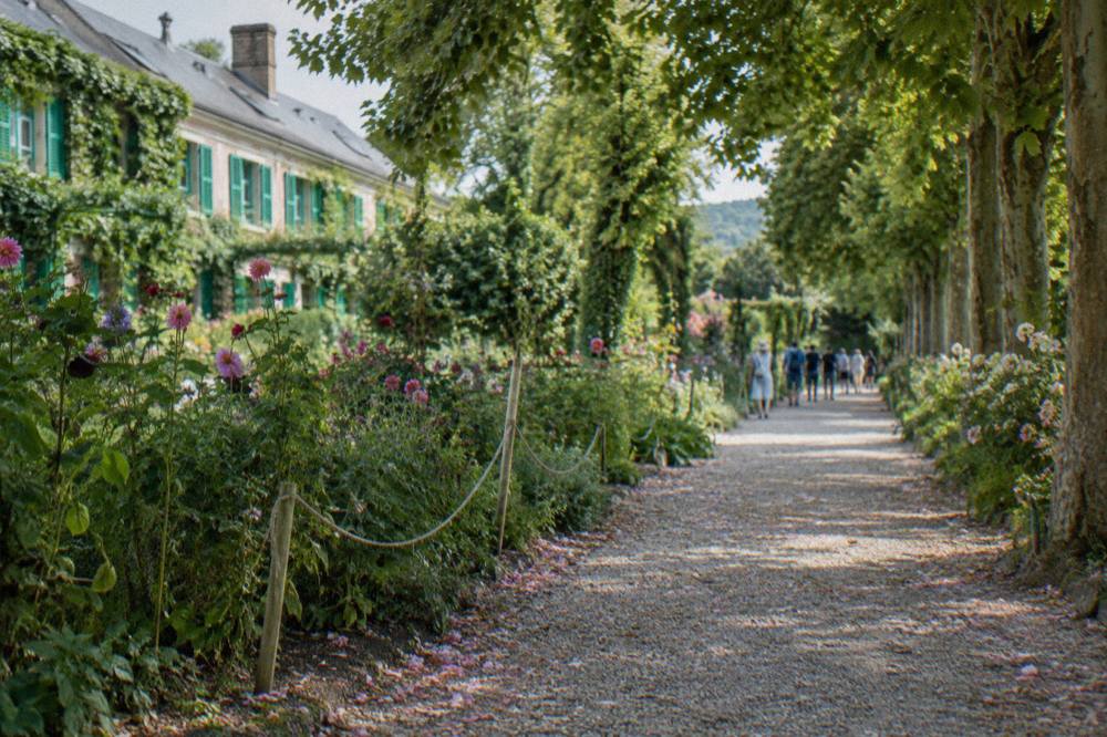 Visitors walking a flower-lined gravel alley in Monet's Clos Normand garden