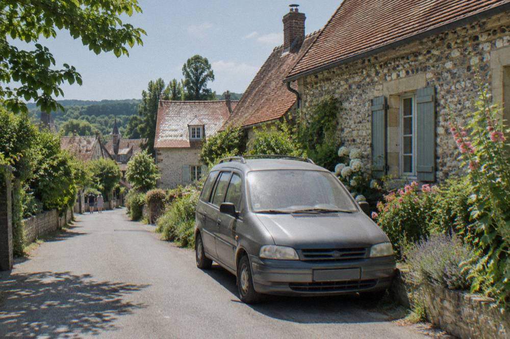 Small minivan parked on a village street beside flower beds in Giverny