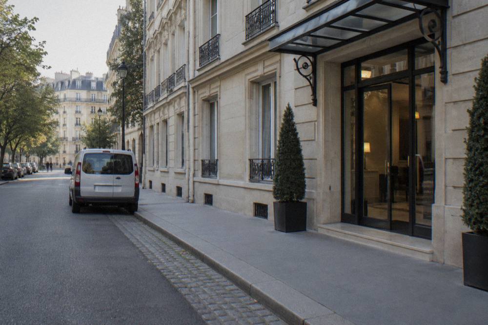 A hotel entrance on a Paris street with a small van waiting at the curb