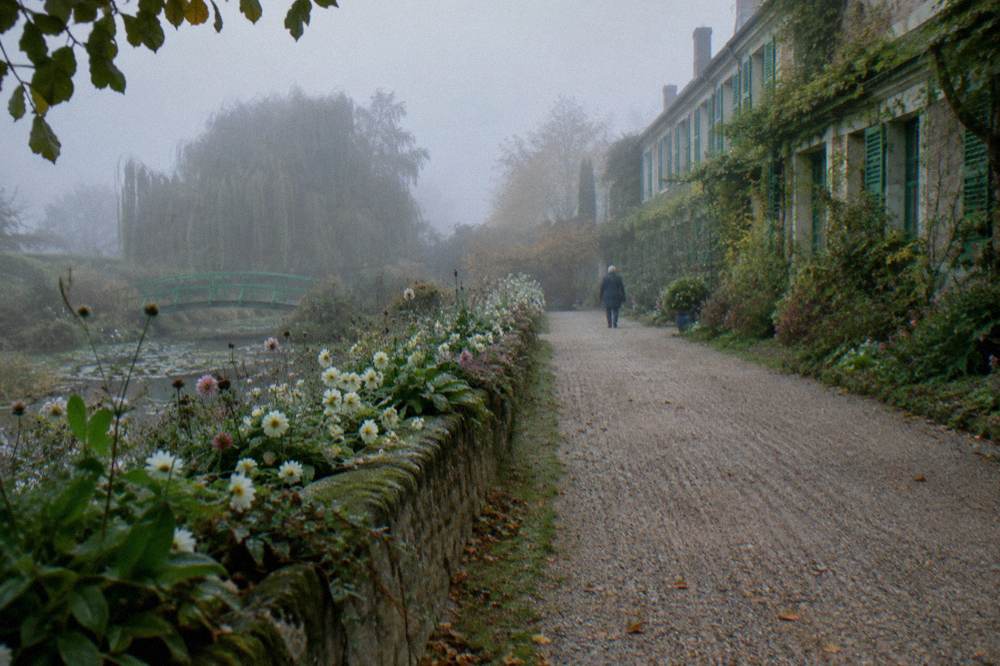 Flower-lined gravel path and stone wall on a quiet morning at Monet's garden in Giverny