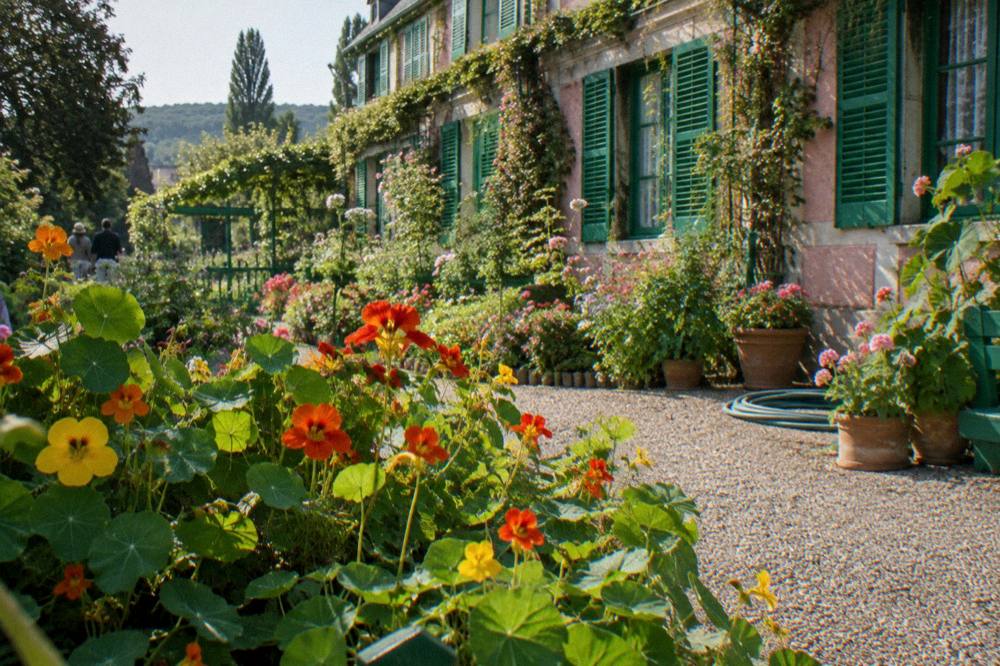 Pink farmhouse facade with green shutters seen from the flower garden at Giverny