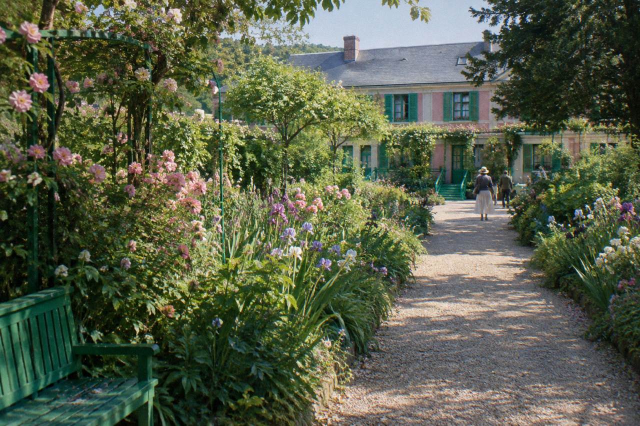 Gravel garden path lined with flowers leading toward Claude Monet's pink house in Giverny
