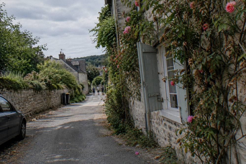 Quiet village lane in Giverny with stone walls and climbing roses in late afternoon light