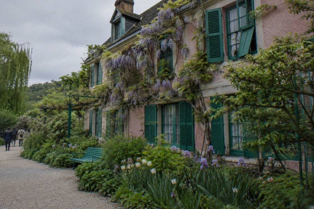 Pink farmhouse facade with green shutters and climbing vines