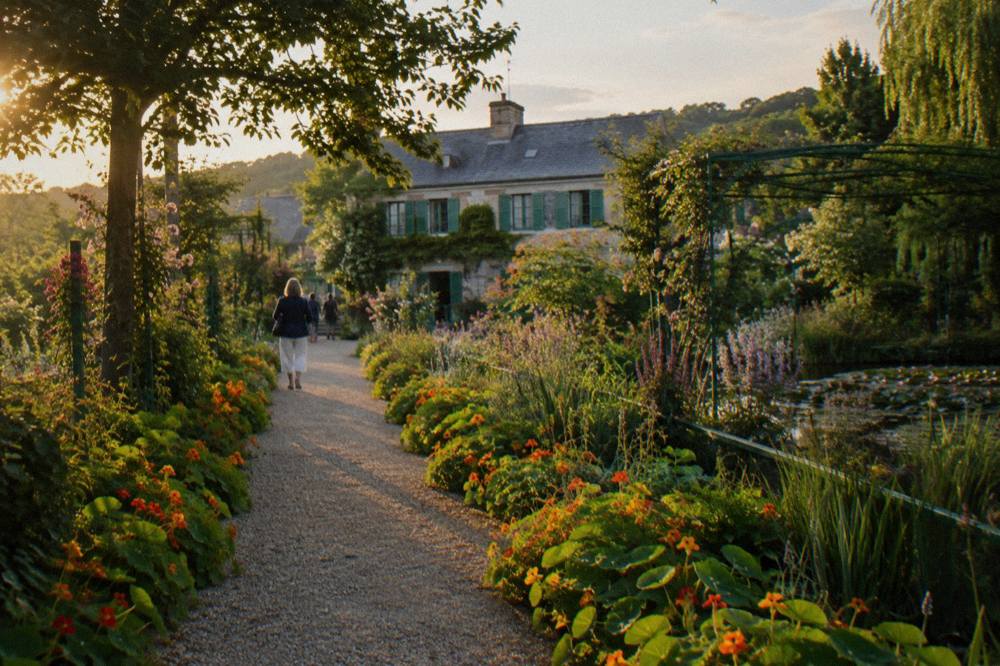 A gravel path lined with flower beds leading toward the pink stone facade of Monet's house