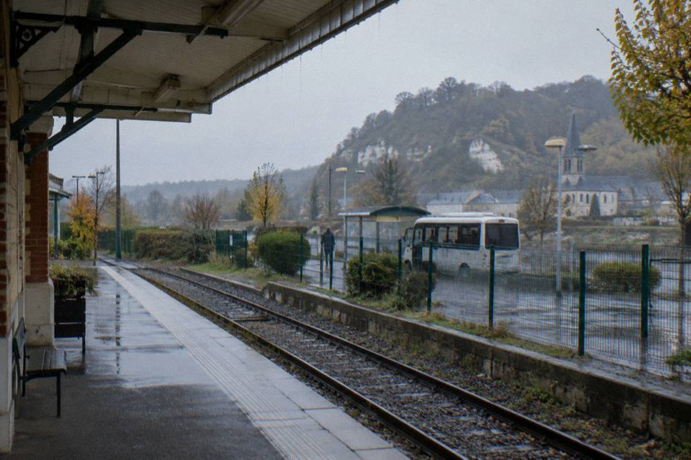 A train platform at Vernon-Giverny station with the village shuttle waiting beyond the fence