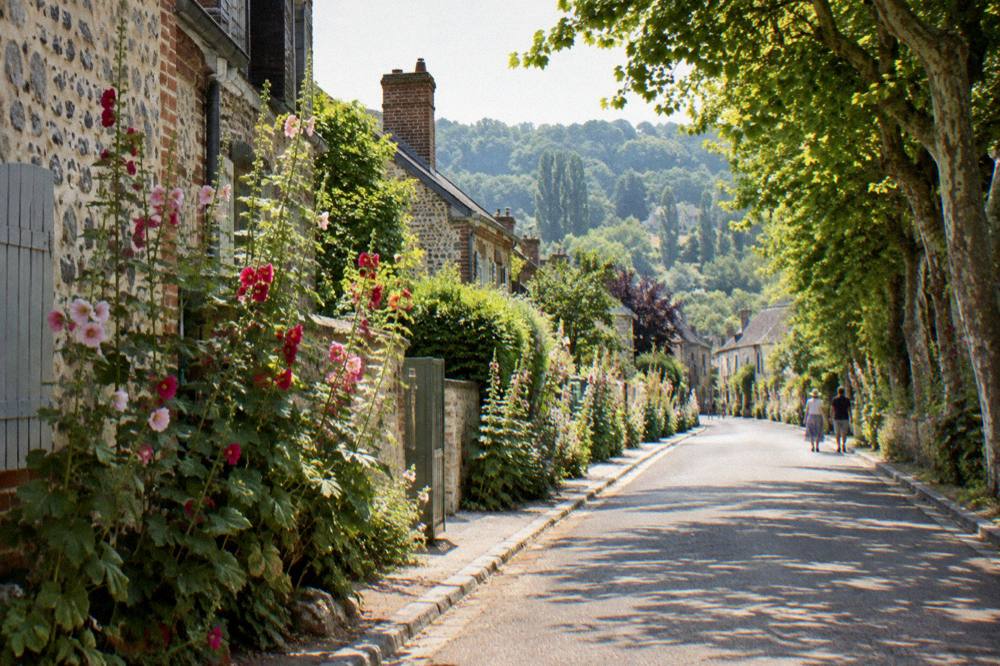 The flower-lined main street of Giverny village with stone buildings under trees