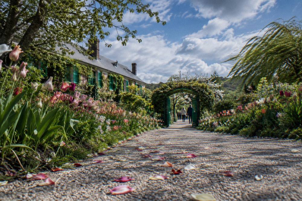 A gravel path lined with flower beds leading toward the entrance of Monet's garden
