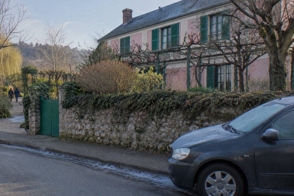 A private car waiting on a village street with the pink facade of Monet's house beyond the garden wall