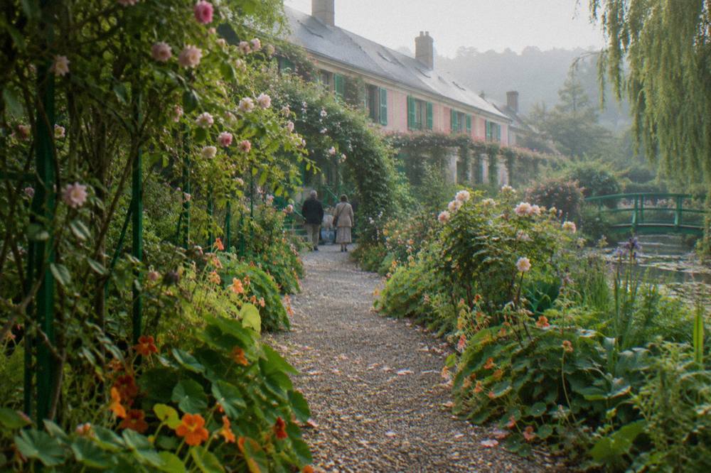 A narrow garden path lined with flowers leading toward Monet's pink house in Giverny