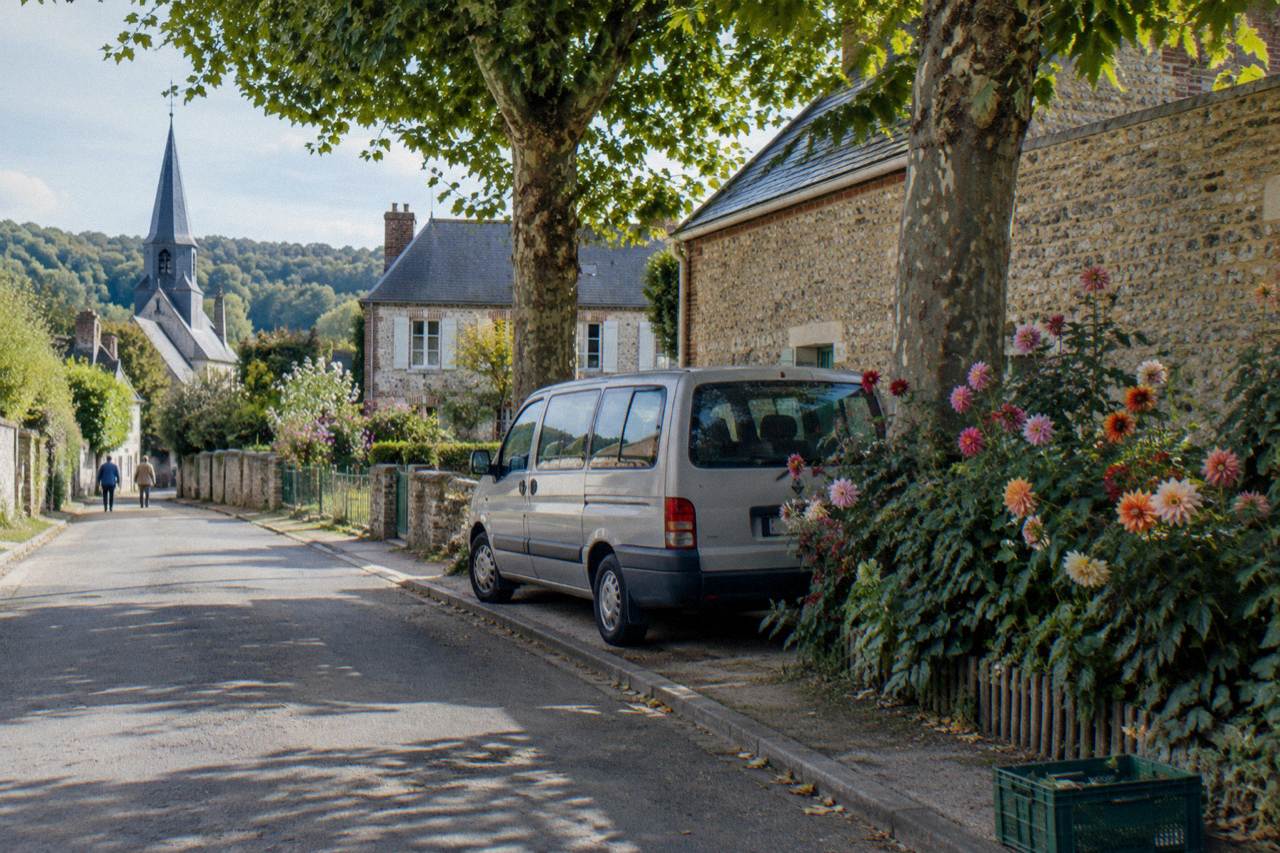 A small minivan parked on a village street beside flower beds near Monet's garden in Giverny