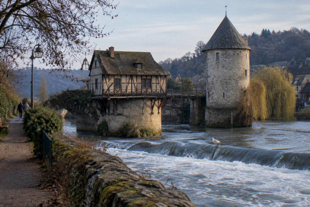 An old timber mill on a stone bridge pier over the Seine beside a round stone tower