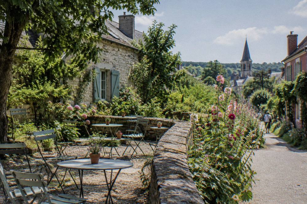 Terrace tables with chairs set beside a flower-lined path near a stone garden wall