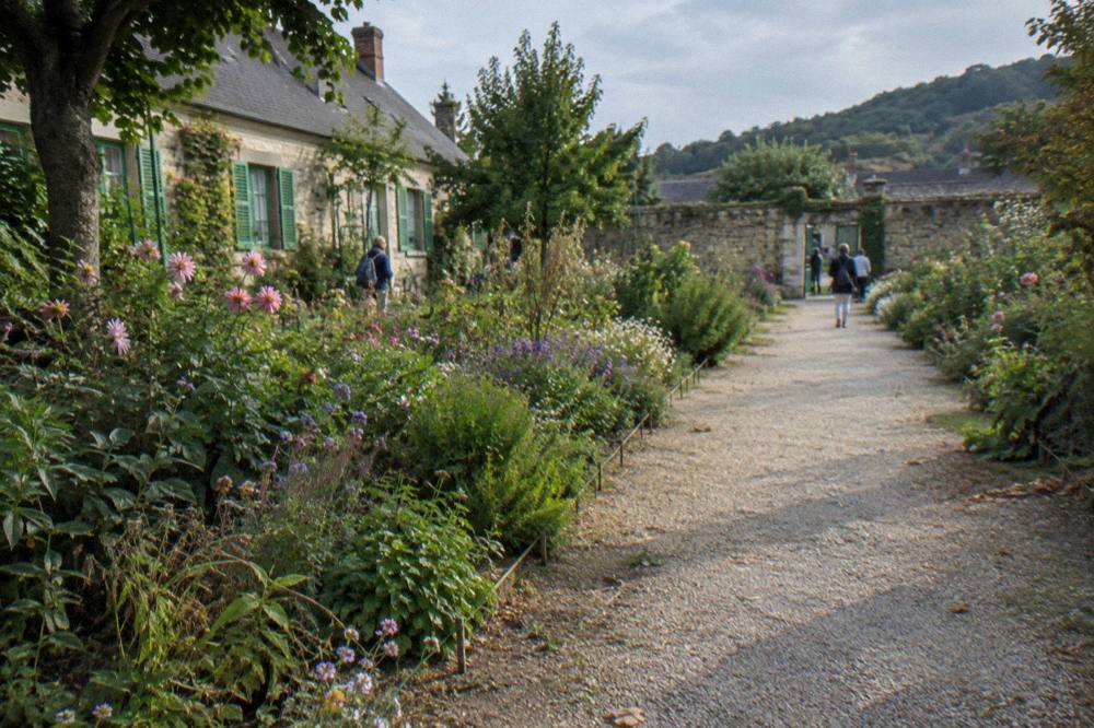 Garden path in late afternoon light with flower borders and distant stone wall
